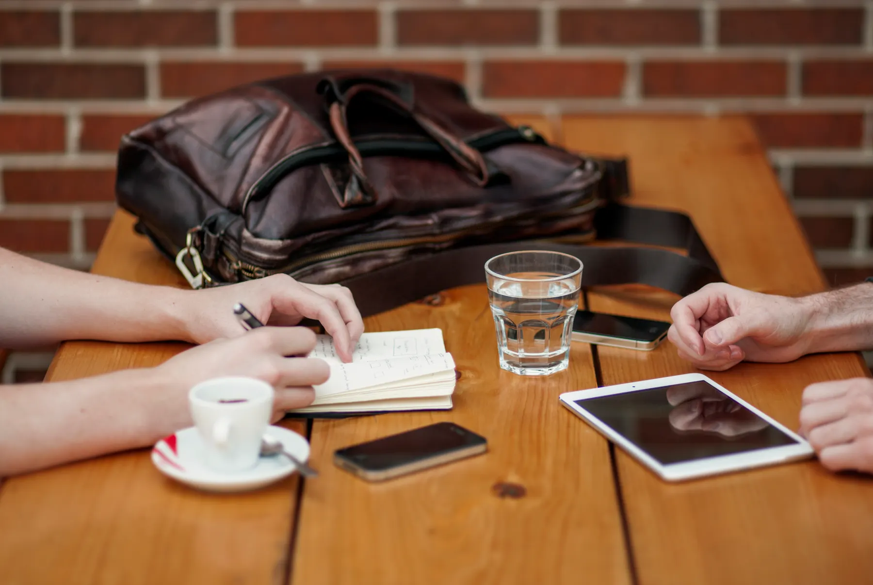 Two people talking across a wooden table with an open notebook and a cup of coffee