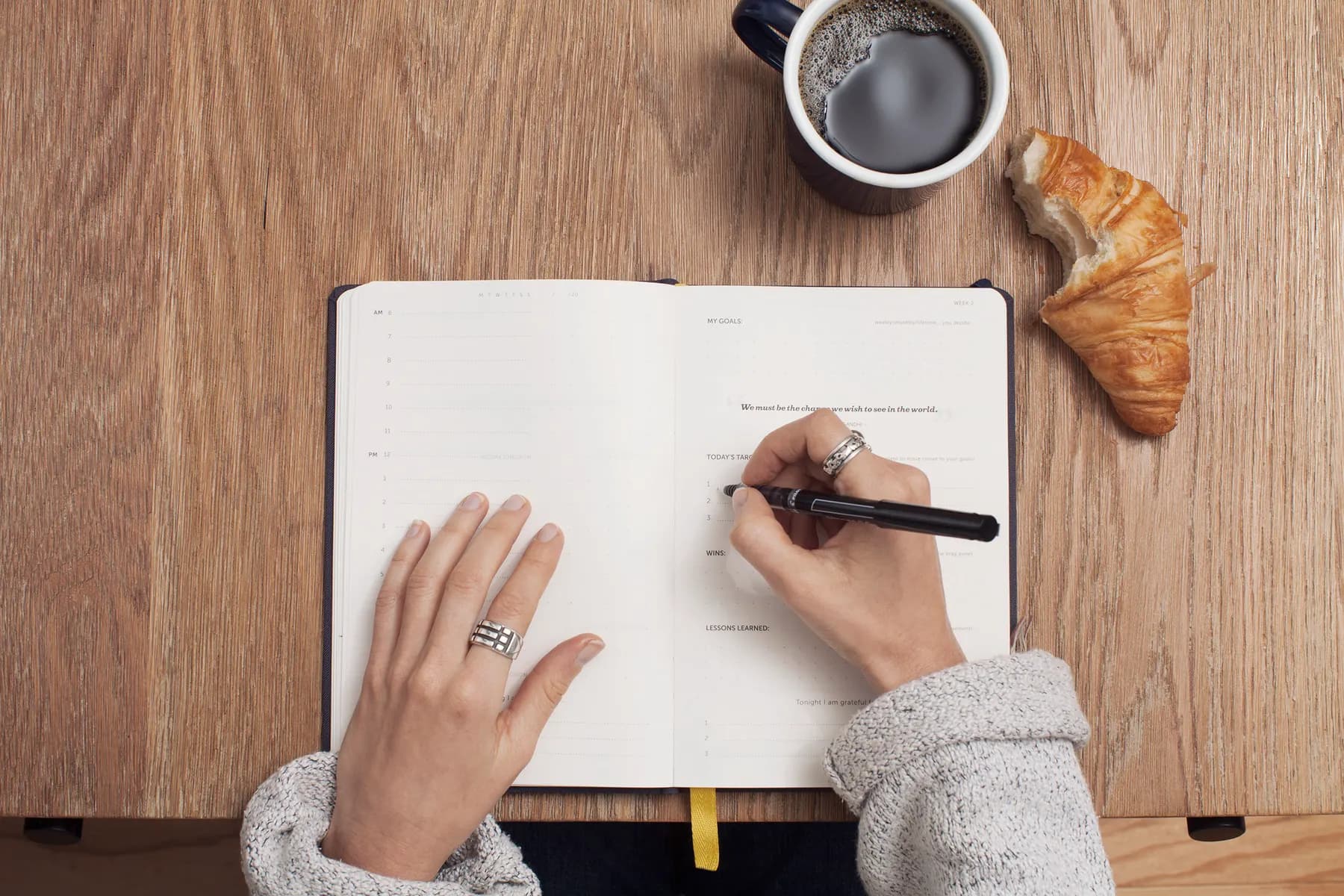 Hands writing goals into a planner beside a cup of black coffee