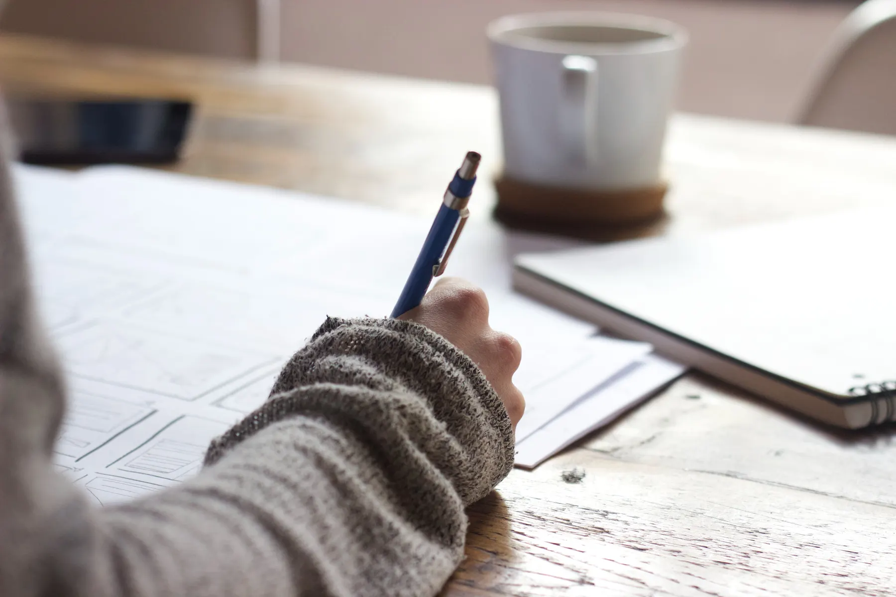 A person sketching out ideas on paper next to a mug of coffee