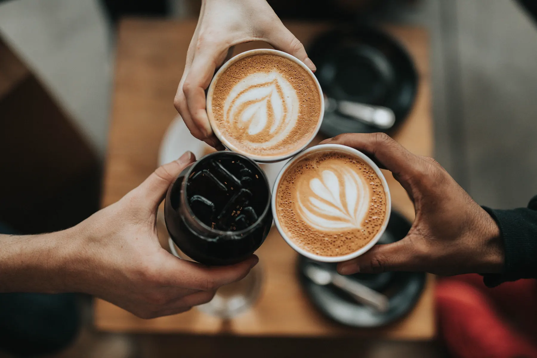 Three people raising coffee cups together over a wooden table